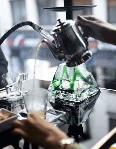 Une chicha moderne avec une base en verre vert, posée sur une table élégante avec une théière argentée et des
